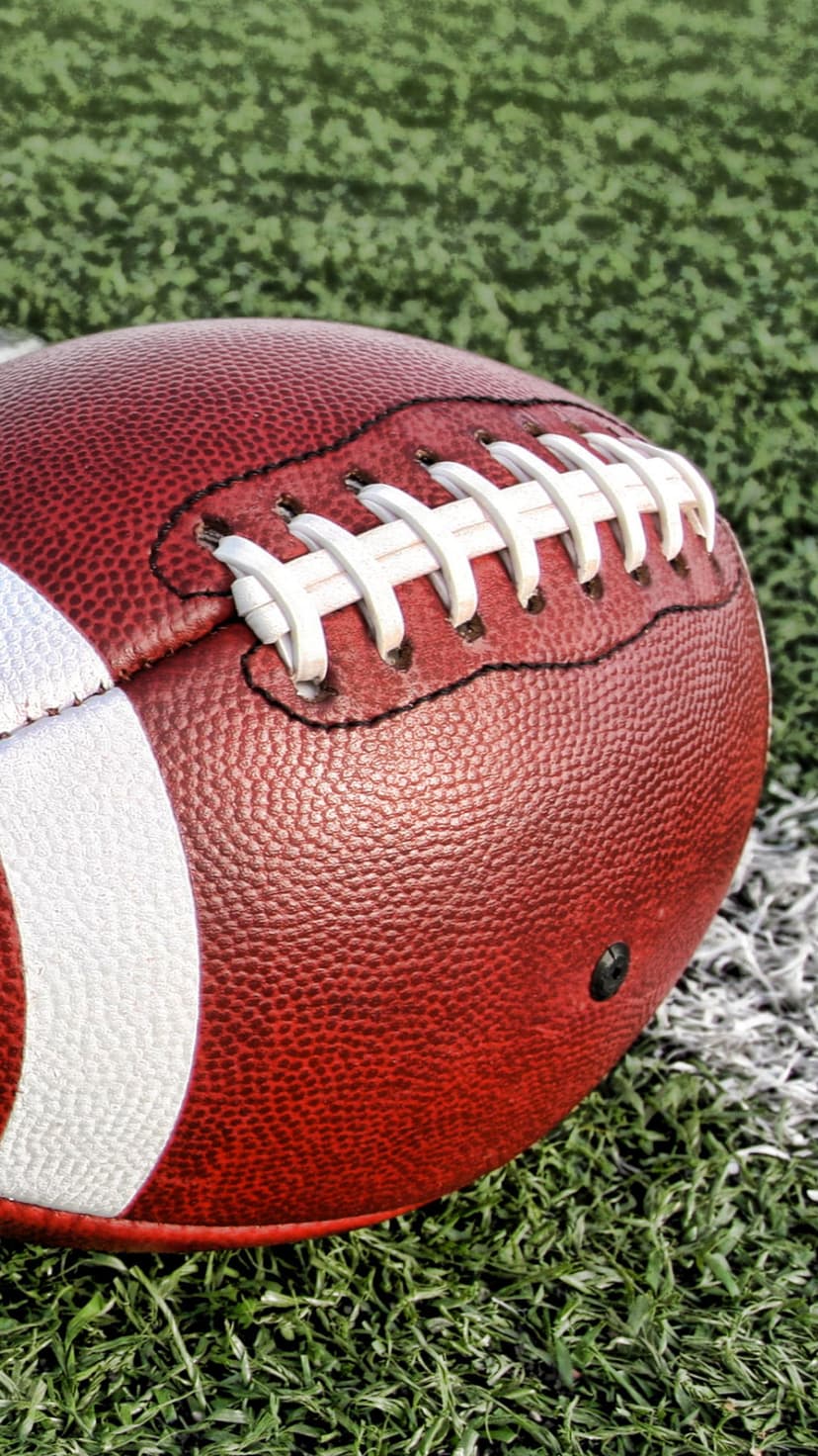 American football with white laces sits on green blades of grass, showing extreme close-up leather texture.