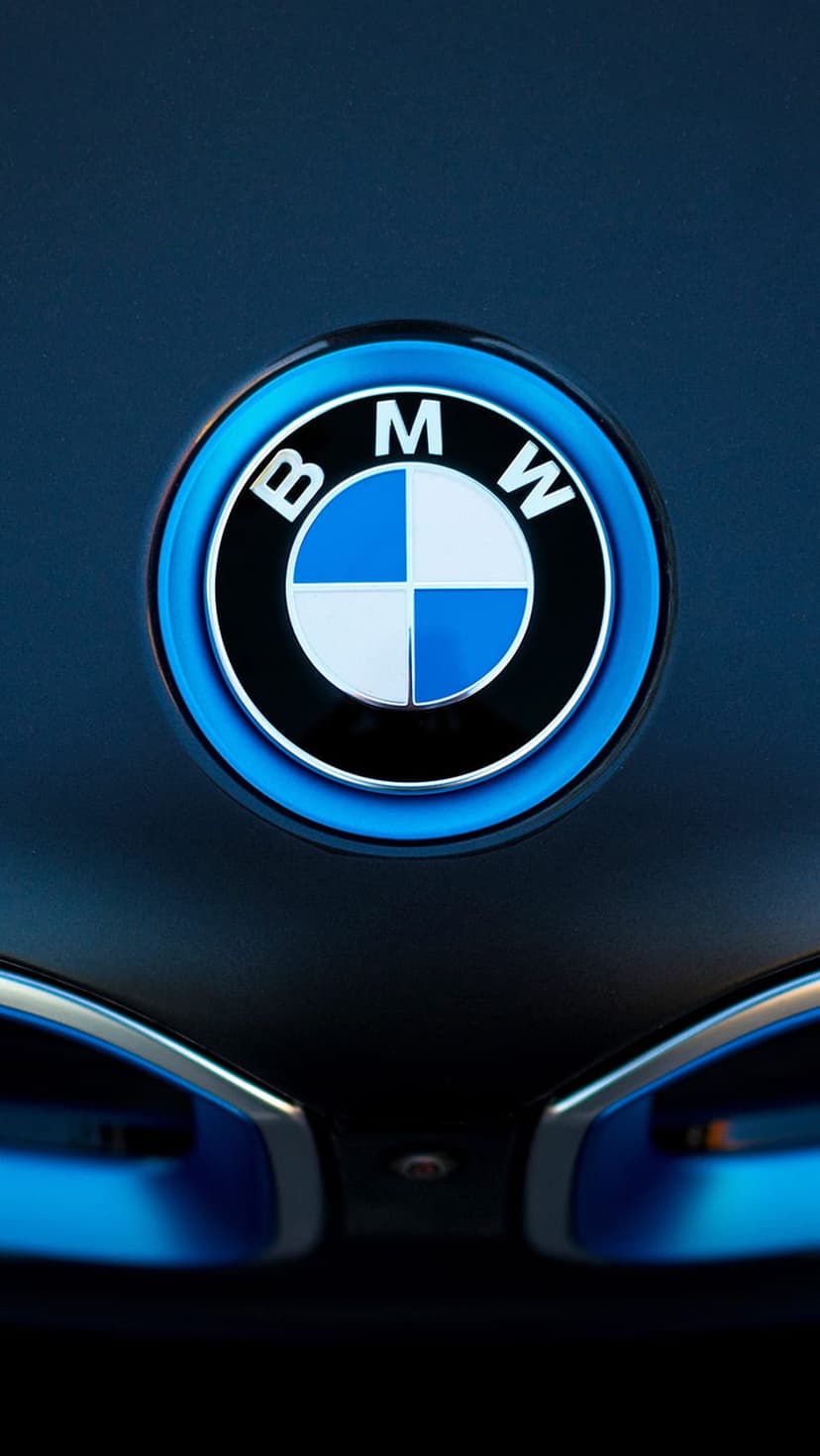 BMW emblem with a glowing blue outer ring centered on a dark car hood under soft ambient LED lighting.