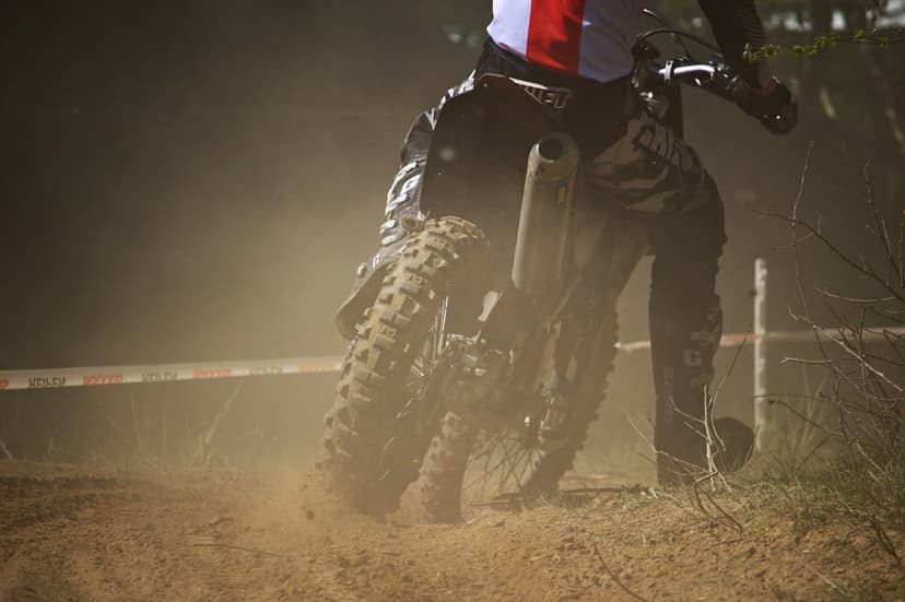 Motocross rider on a dirt bike kicks up a cloud of dust on a sandy racing track with a blurred background.