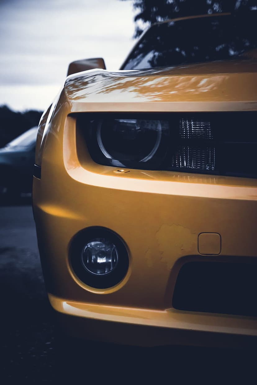 Yellow Chevrolet Camaro headlight and fog light featuring metallic paint reflections on a vertical wallpaper.