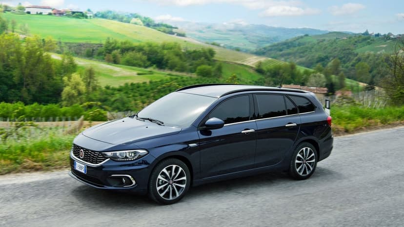 Dark blue Fiat Tipo Station Wagon driving on a scenic road with rolling green hills in the background.