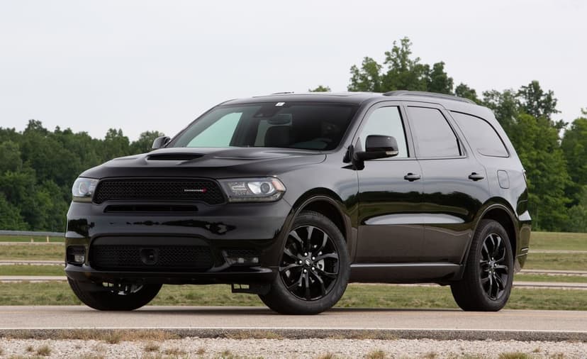 Black Dodge Durango performance SUV with black wheels on a road against a backdrop of green forest trees.