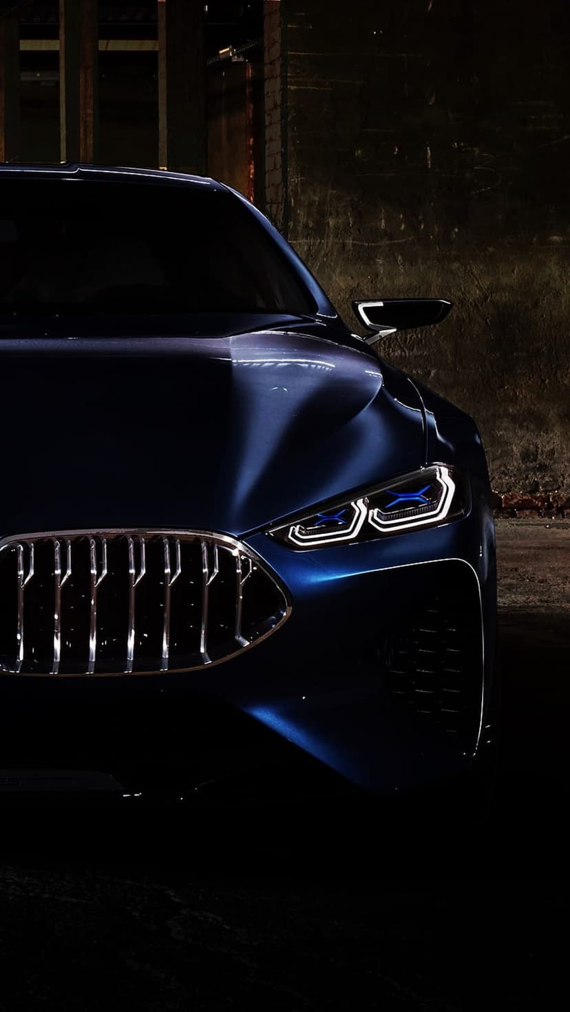 BMW front grille and sharp LED headlights with blue accents glow against a dark, out-of-focus background.