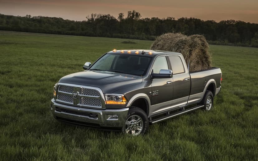 Dark gray pickup truck with a large hay bale in the bed parked in a tall grassy field under a warm sunset sky.