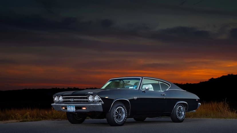 Black 1969 Chevrolet Chevelle SS 396 parked on a road during a dramatic orange and dark blue sunset.