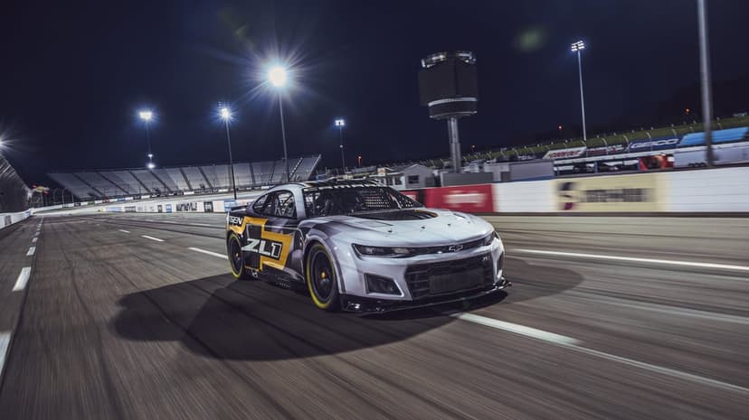 Chevrolet Camaro ZL1 Next Gen race car speeds along a track at night under bright stadium floodlights.
