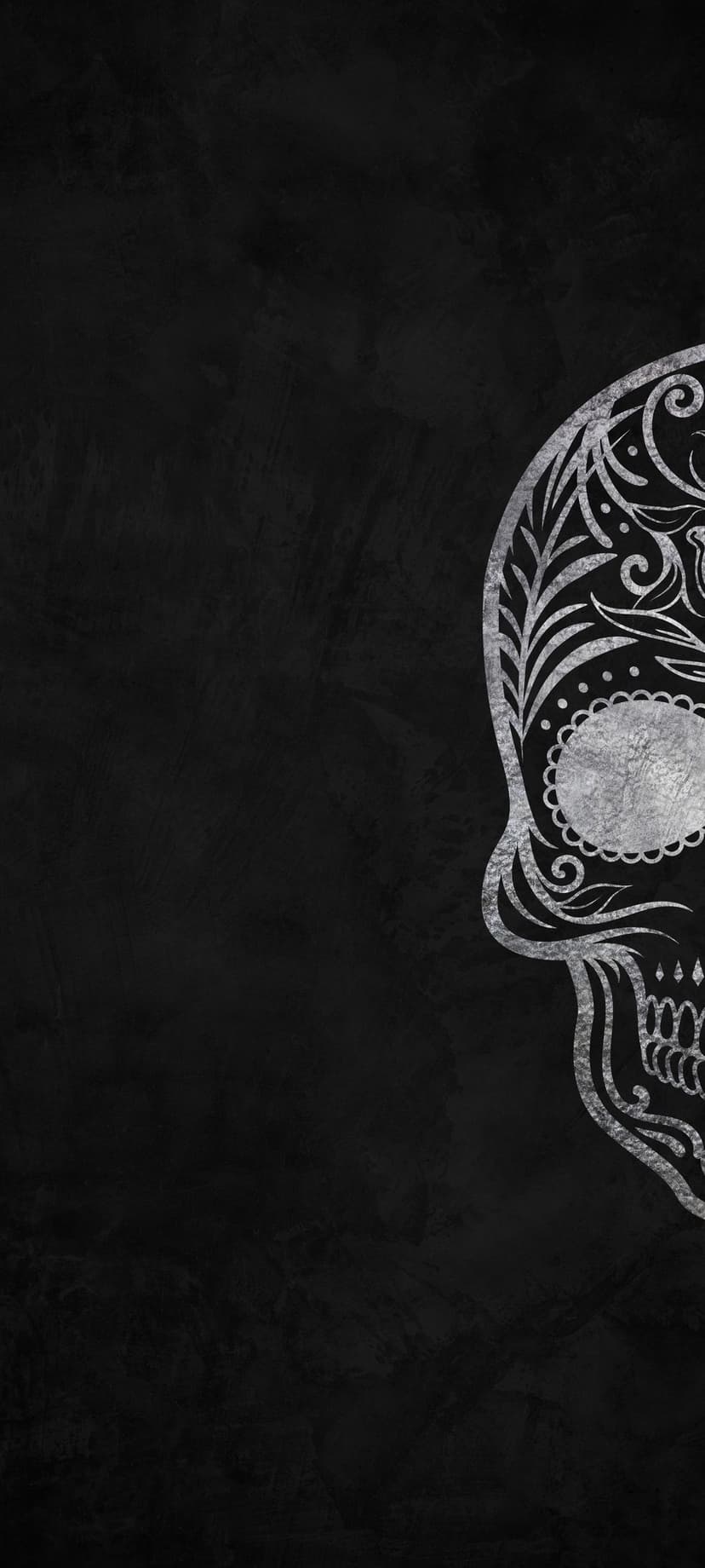 Silver sugar skull with intricate floral engravings and scrollwork patterns on a dark, textured background.