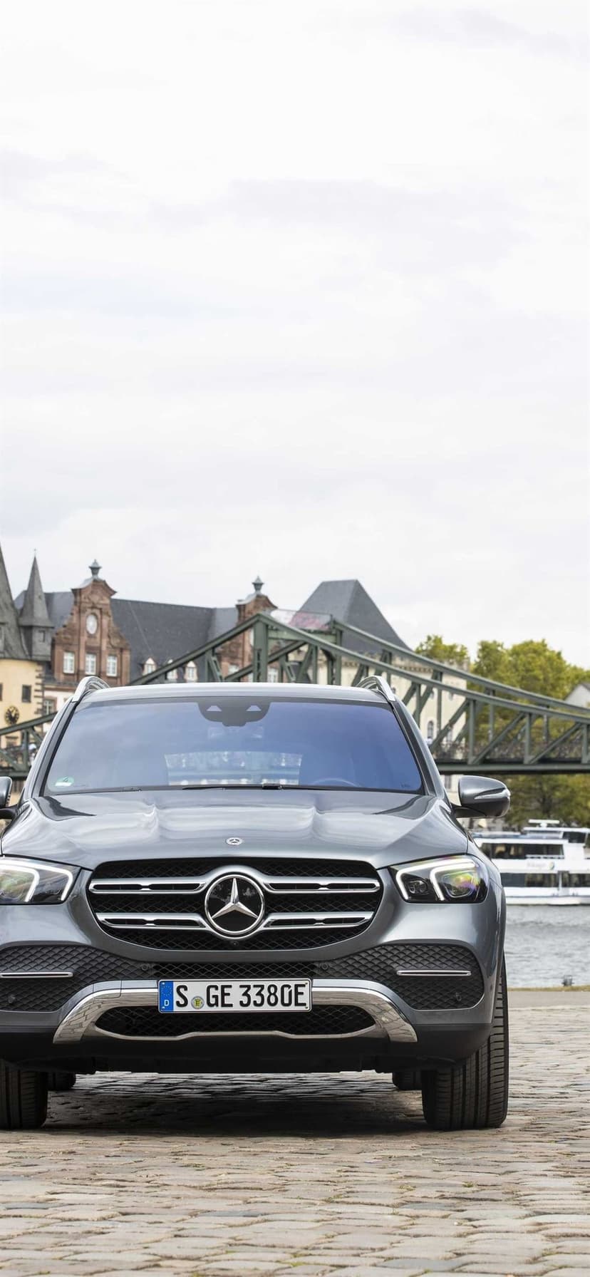 Front view of a grey Mercedes-Benz SUV on cobblestones with the green Iron Bridge and city buildings behind.