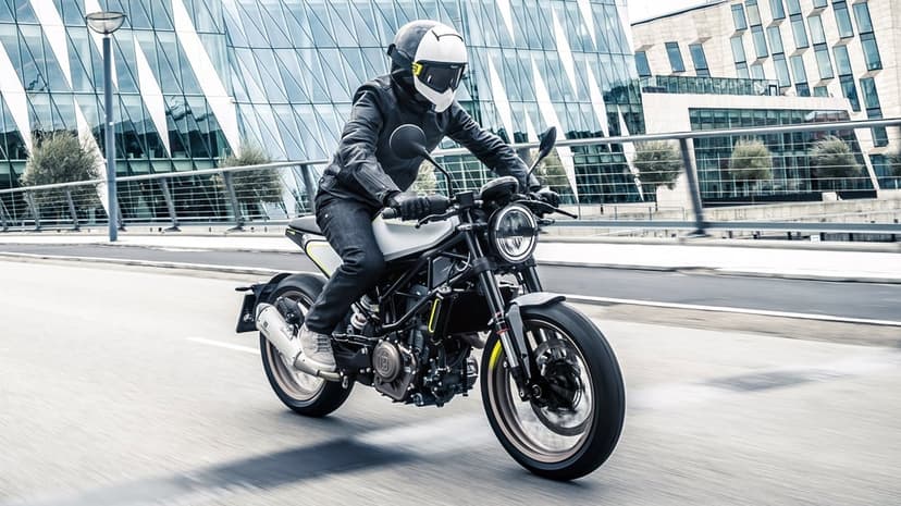 Husqvarna motorcycle rider in a white helmet speeding past modern glass buildings on a gray city street background.