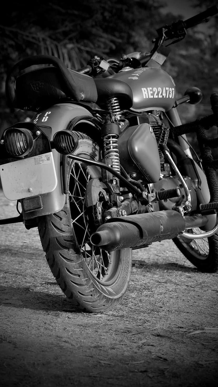 Rear wheel and exhaust of a vintage motorcycle showing wire spokes, tire tread, and a small taillight in B&W.