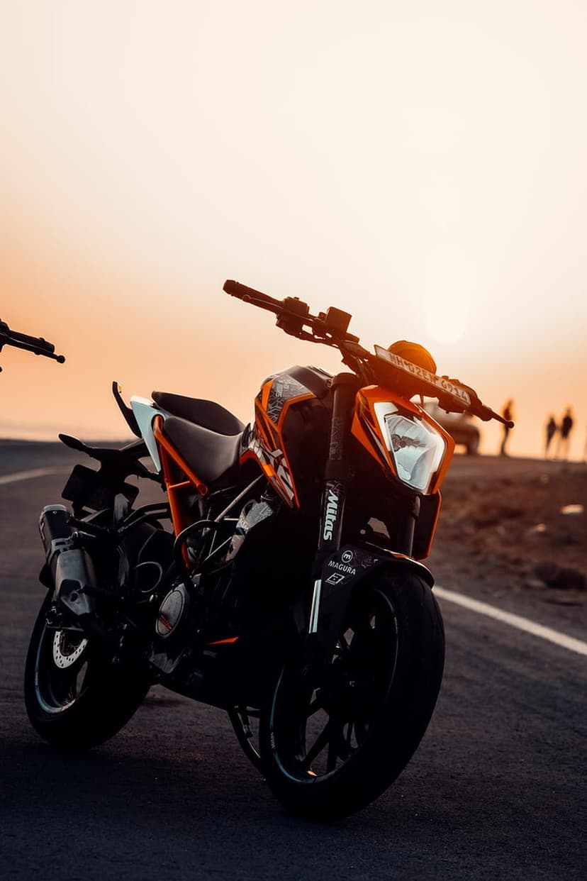 KTM motorcycle with orange and black accents parked on a road during golden hour with a hazy sunset background.