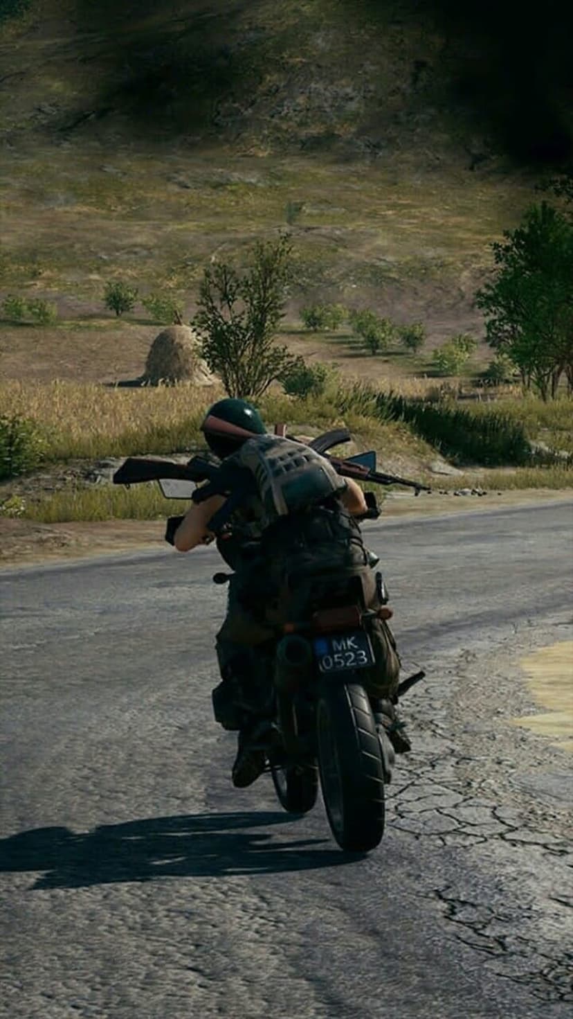 Soldier in tactical gear holding a rifle while riding a motorcycle on a cracked asphalt road in the countryside.