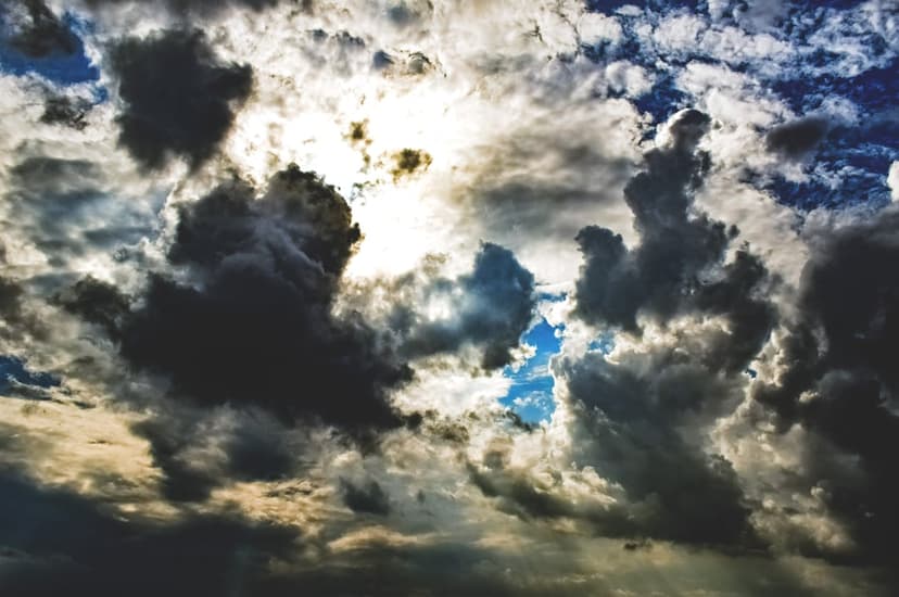Golden sunbeams pierce through heavy dark storm clouds with patches of bright blue sky showing through gaps.