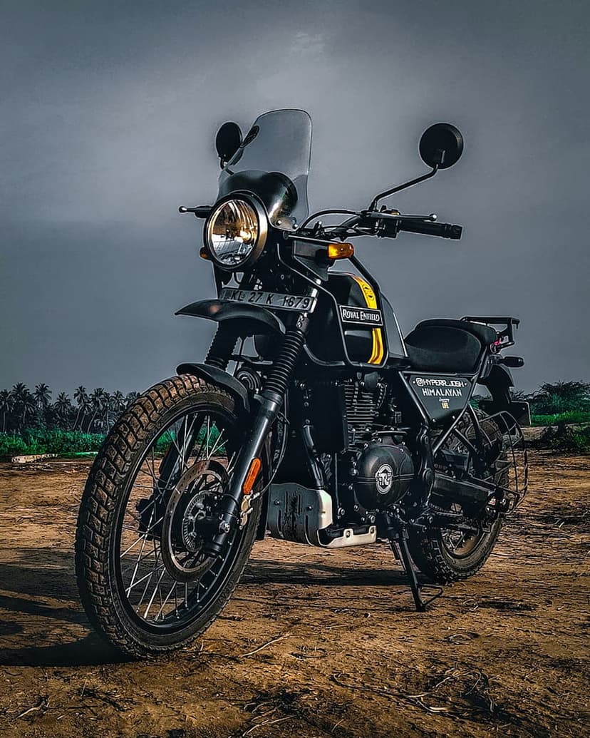 Royal Enfield Himalayan motorcycle on a dusty trail with knobby tires and a round headlamp under an overcast sky.