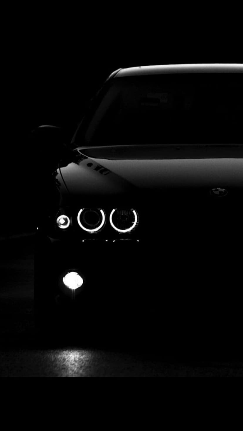 BMW front fascia with illuminated circular halo headlights and fog lights against a deep black background.