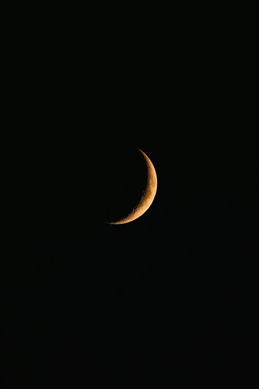 Golden crescent moon with visible crater textures suspended in a pitch black night sky, centered vertically.