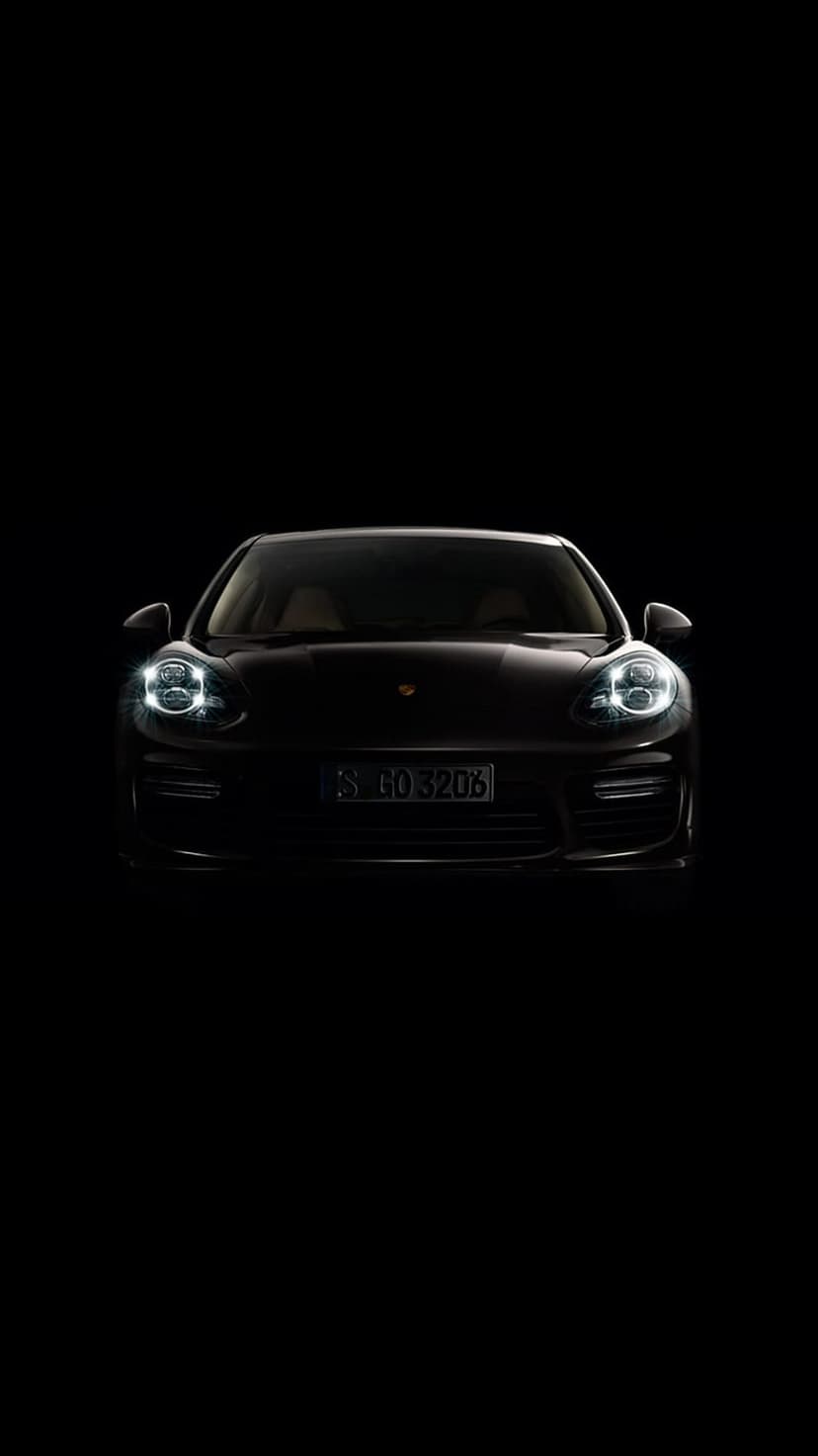 Porsche Panamera front grille and glowing LED headlights emerge from a pitch-black studio background.