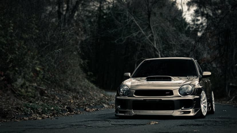 Subaru Impreza WRX STI with white wheels parked on a dark, tree-lined road in a cinematic forest setting.