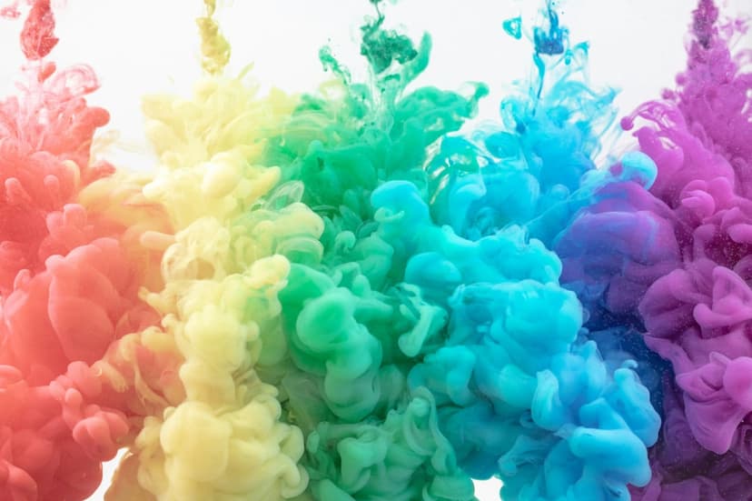 Rainbow-colored ink plumes swirl through water with vibrant red, yellow, blue, and purple pigments in motion.