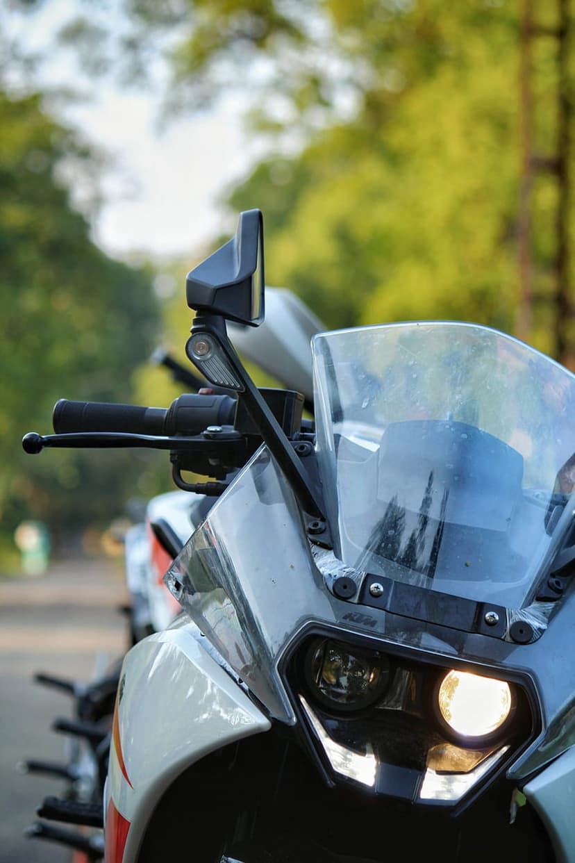 KTM motorcycle headlight and side mirror with a glowing LED bulb against a blurred green leafy background.