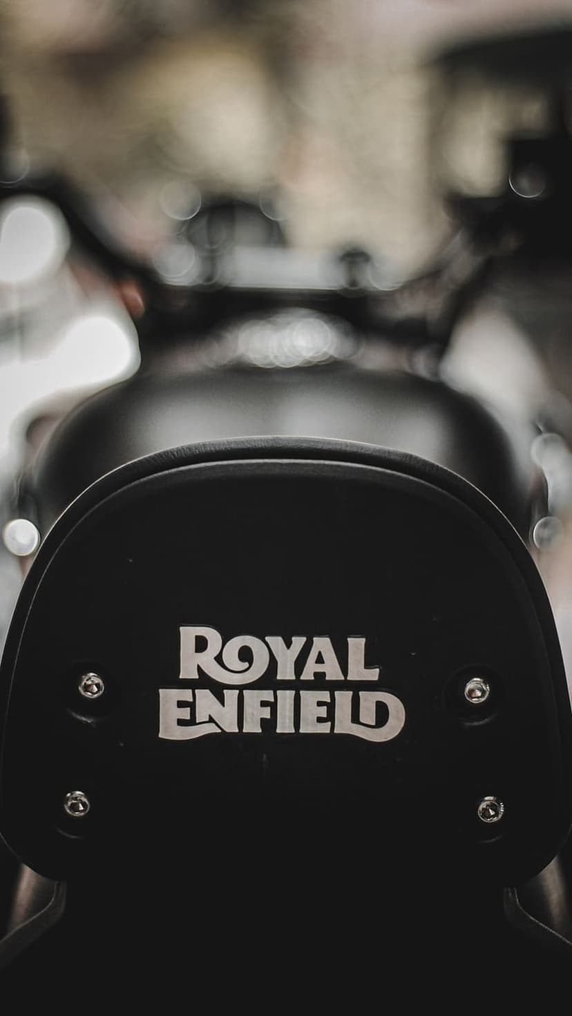 Royal Enfield silver metallic logo embossed on a black leather motorcycle seat backrest with blurred background.