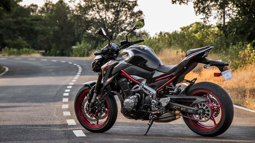 Black Kawasaki Z900 motorcycle with red wheels on a curved forest road with golden hour lighting and bokeh.