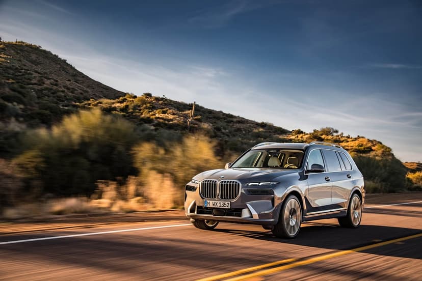 A grey BMW X7 SUV drives on a desert highway during golden hour with blurred mountains in the background.