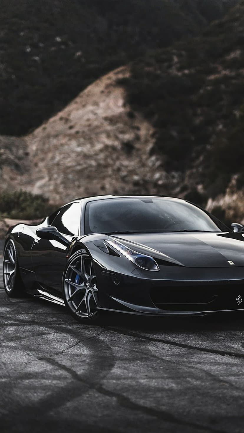 Black Ferrari 458 Italia parked on a cracked asphalt road with blurred mountains under moody twilight skies.