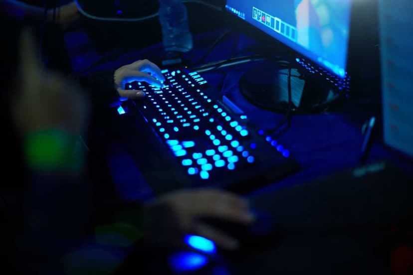 Person's hands using a glowing blue backlit mechanical keyboard and mouse in a dark immersive gaming setup.