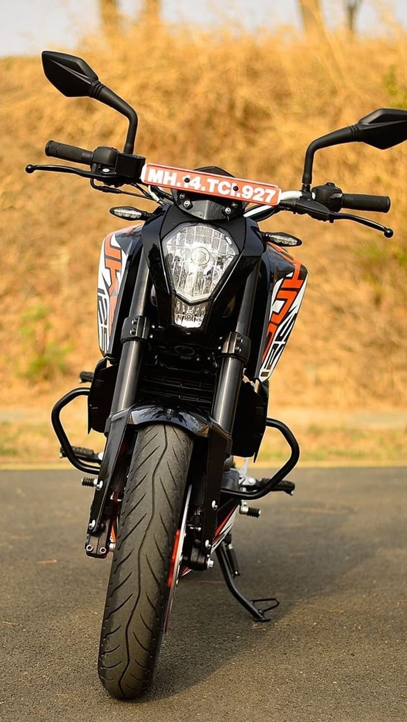 KTM 390 Duke motorcycle front headlight and handlebars parked in a field with blurred dry grass background.