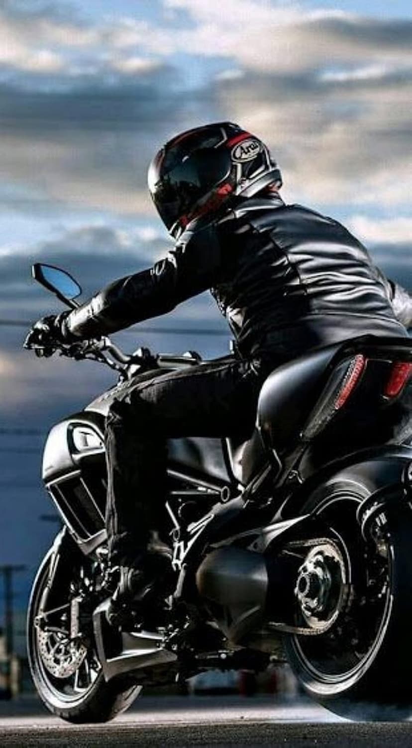 Motorcyclist in black leathers riding a Ducati sportbike against a cloudy dusk sky with a visible taillight glow.