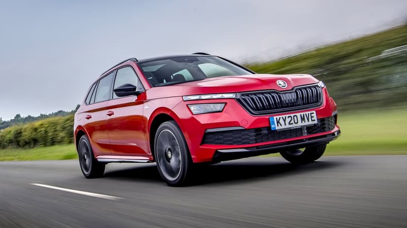 Red Skoda Kamiq SUV driving on a paved road with motion blur against a green landscape and grey sky.