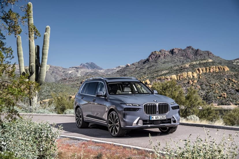 Grey BMW X7 luxury SUV on a desert road with mountains and saguaro cacti under a clear blue sky.