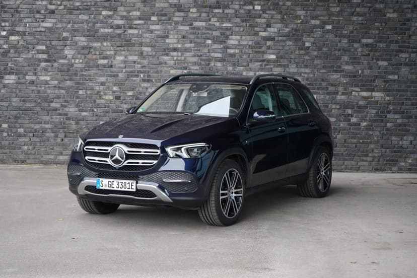 Dark blue Mercedes-Benz GLE SUV parked in front of a gray brick wall with chrome grille accents visible.