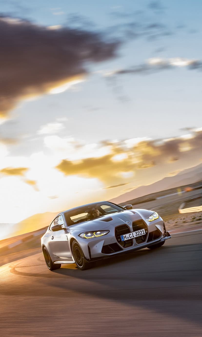 Silver BMW M4 CSL drifting on a track at sunset with motion blur and warm golden lighting.