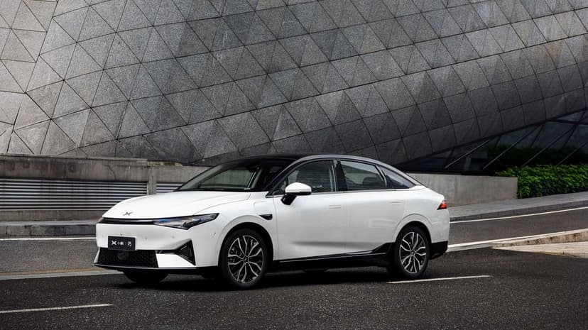 White Xpeng P5 electric car parked on a road beside a large grey building with geometric triangular textures.
