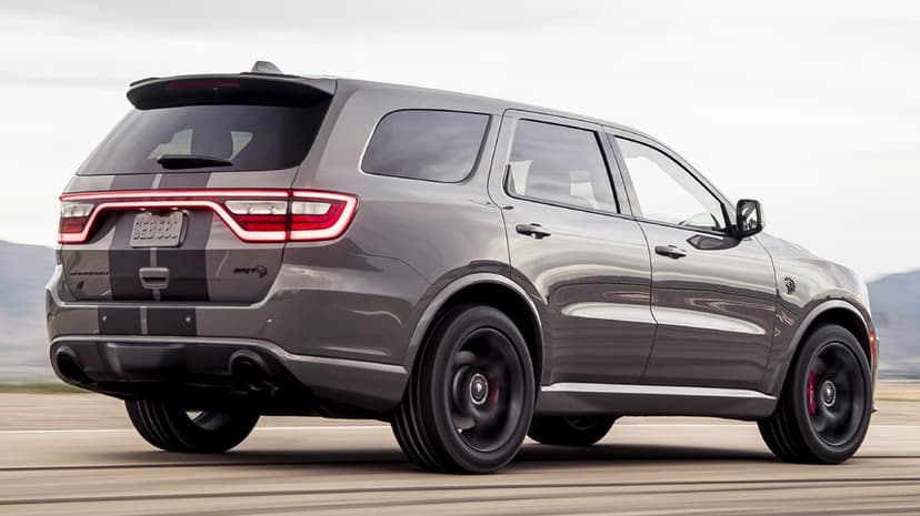 Grey Dodge Durango SRT Hellcat with black stripes and red taillights driving at high speed on an open track.