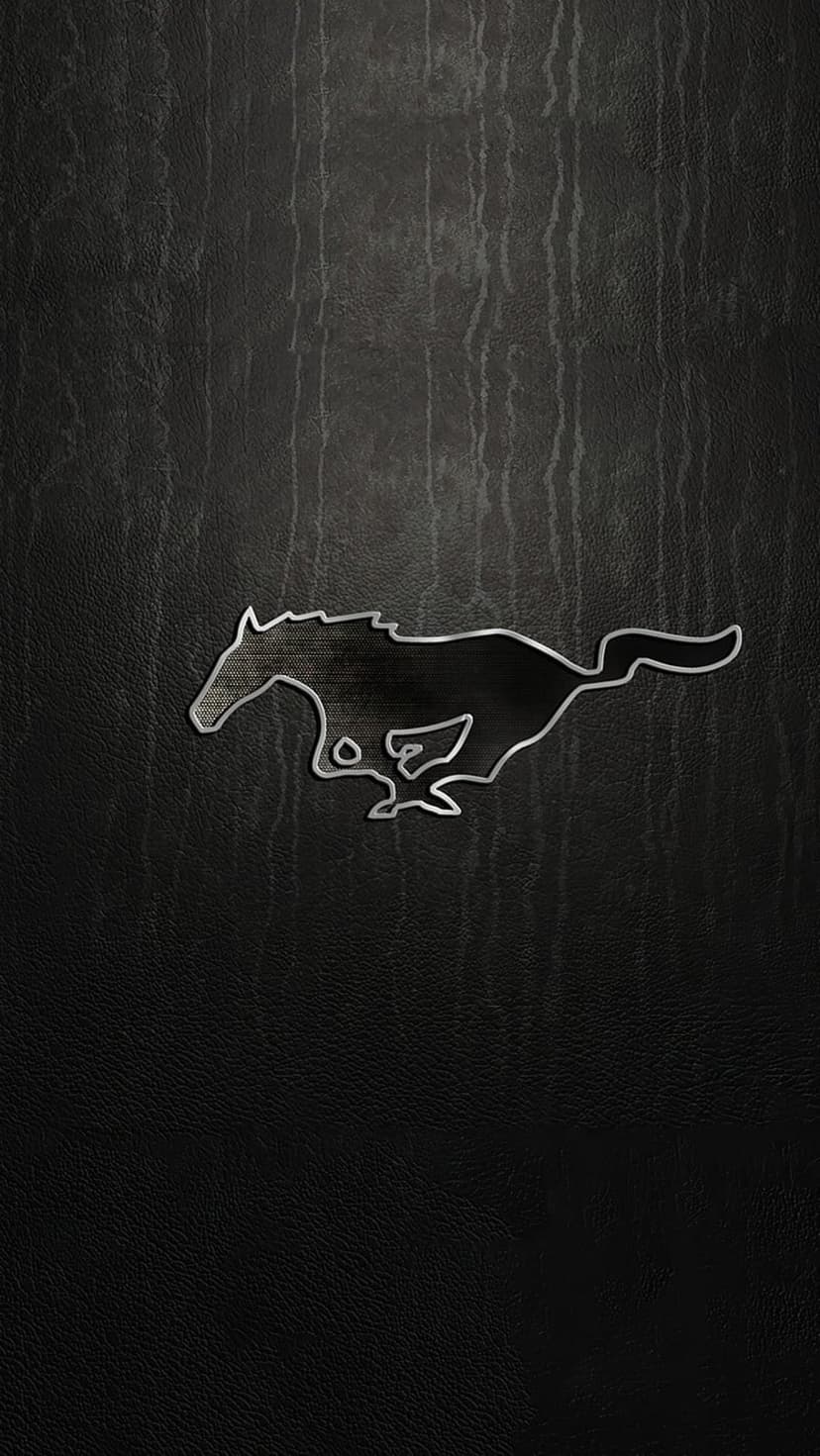 Silver galloping Mustang logo centered on a black textured leather surface with vertical grain and soft shadows.