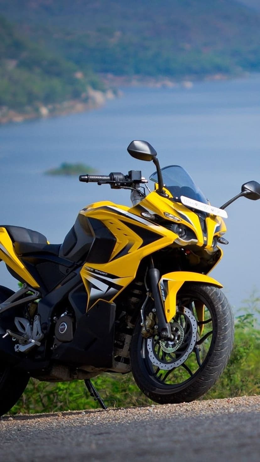 Yellow sport motorcycle with black accents parked on gravel beside a calm lake and distant rolling hills.