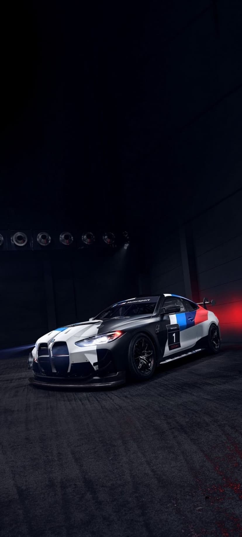 BMW M4 GT3 race car with black and white camouflage livery and number one decal in a dimly lit studio.