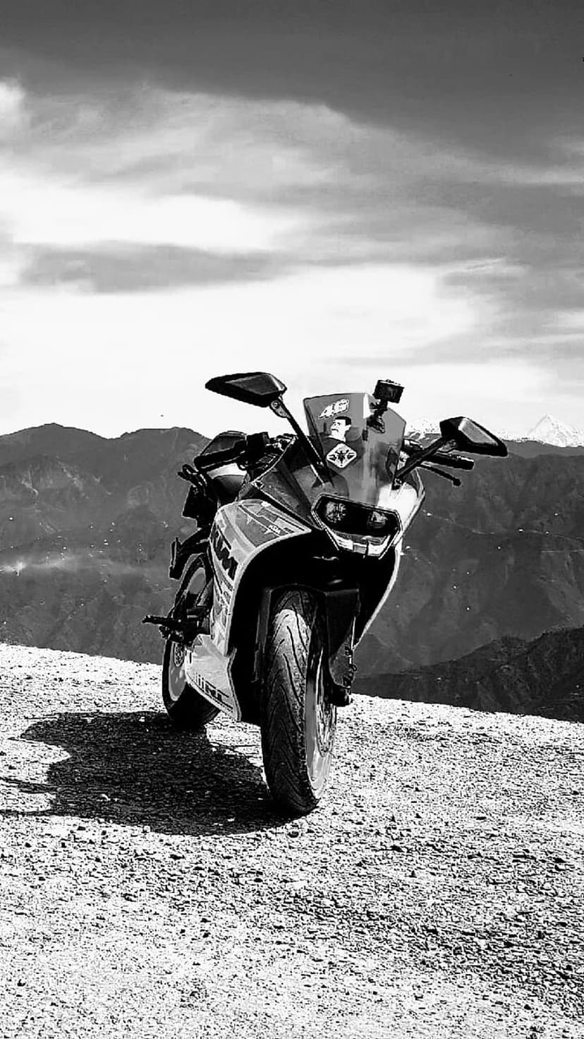 Sport motorcycle on a gravel mountain path under a cloudy sky in a monochrome vertical composition.