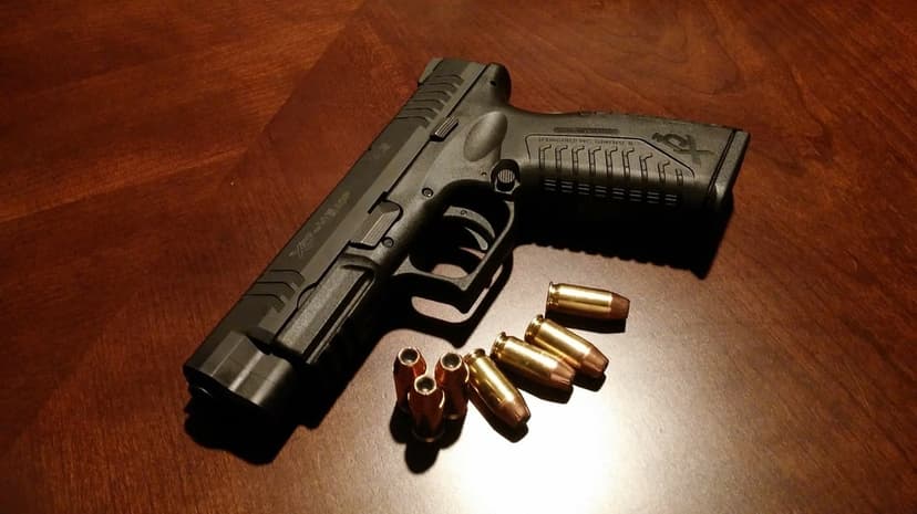 Black semi-automatic handgun and brass ammunition resting on a polished dark wood table with dramatic shadows.