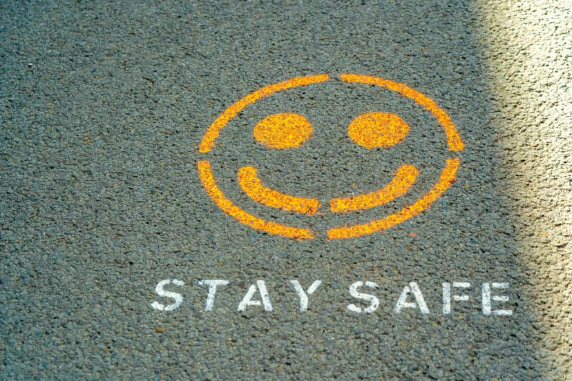 Vibrant orange smiley face stencil with white Stay Safe text on dark asphalt pavement with soft shadows.