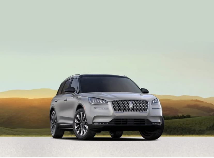 Silver Lincoln Corsair SUV parked on a road with golden hills and a soft sunset sky in the background.