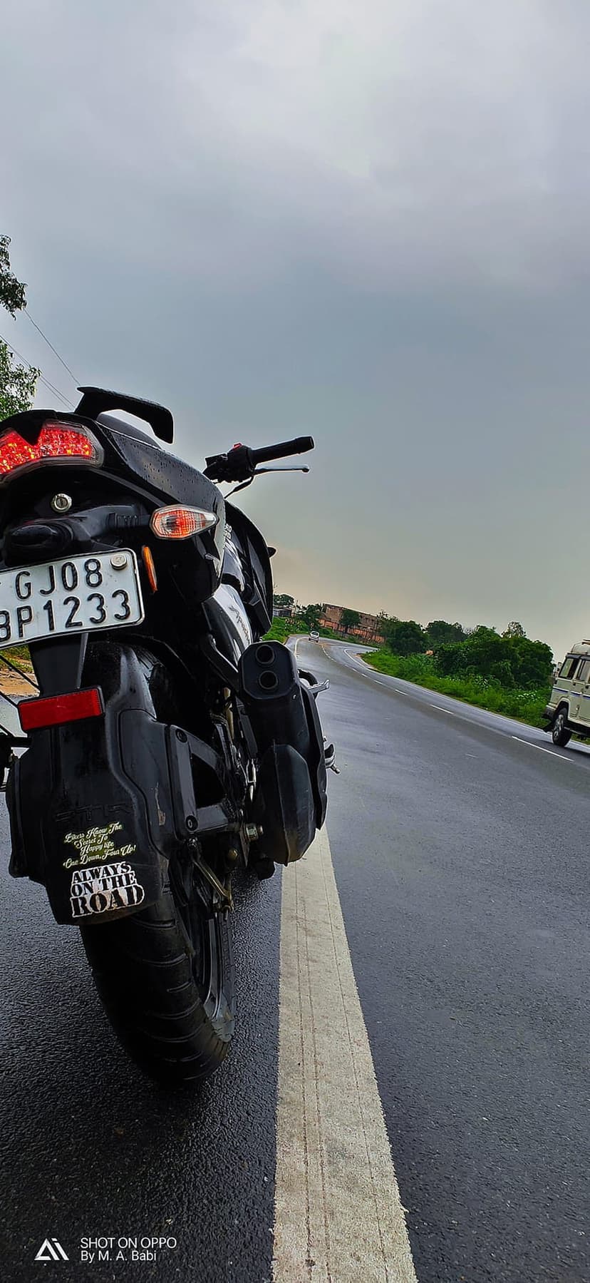 Black motorcycle parked on wet asphalt under a dark cloudy sky with a visible sticker on the rear fender.