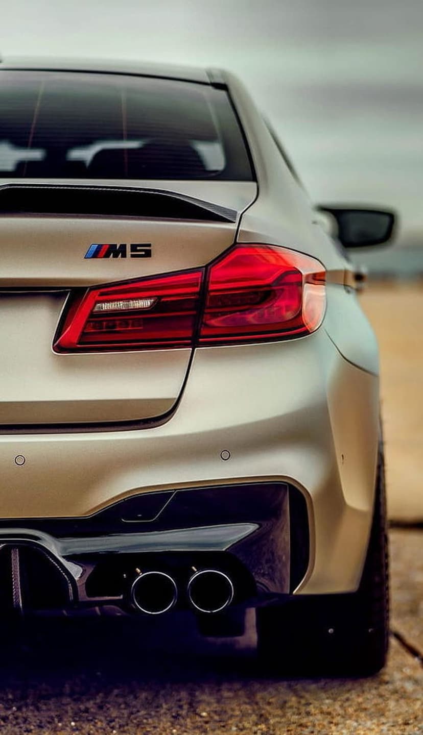 BMW M5 rear end featuring red LED taillights, chrome quad exhaust tips, and a matte black diffuser detail.