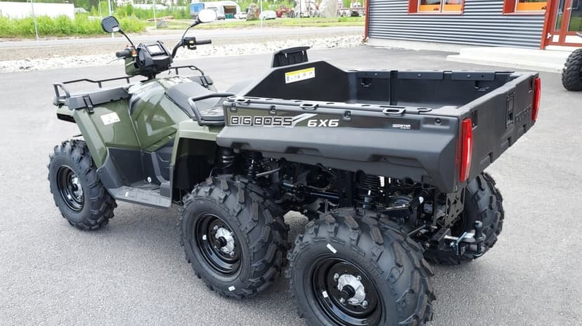 Olive green 6x6 utility ATV with a rear cargo bed and knobby tires parked on a grey asphalt lot.