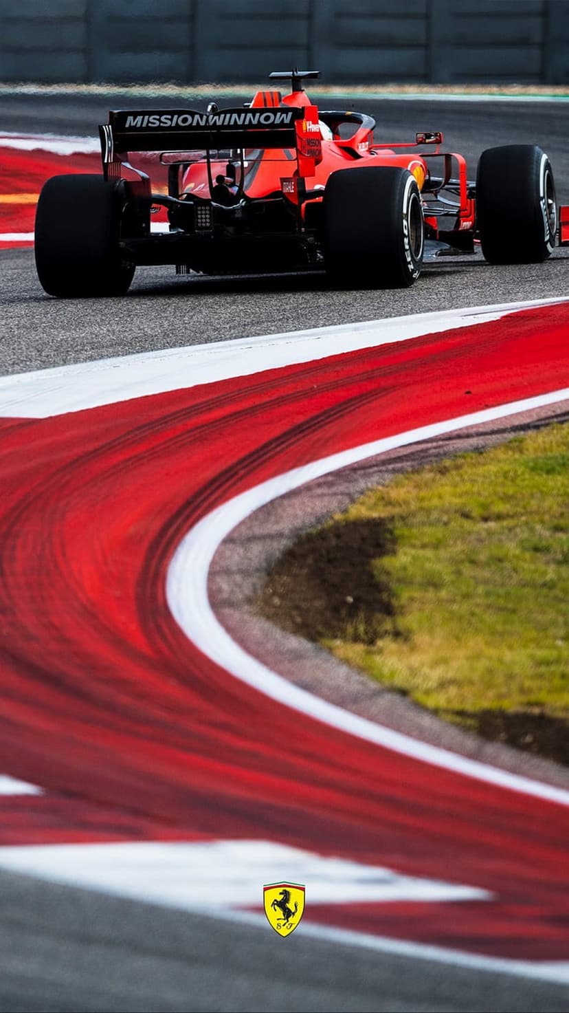 Red Ferrari F1 car rear wing and tires speeding past striped track kerbs with tire marks on the asphalt surface.