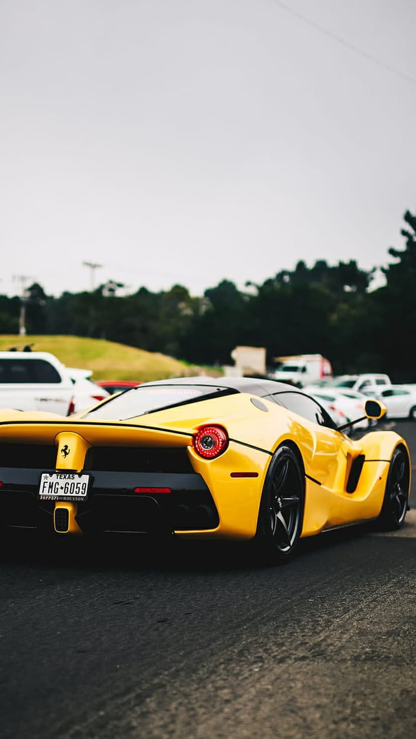 Yellow Ferrari LaFerrari rear view showing round taillights and a Texas license plate on a gray asphalt surface.