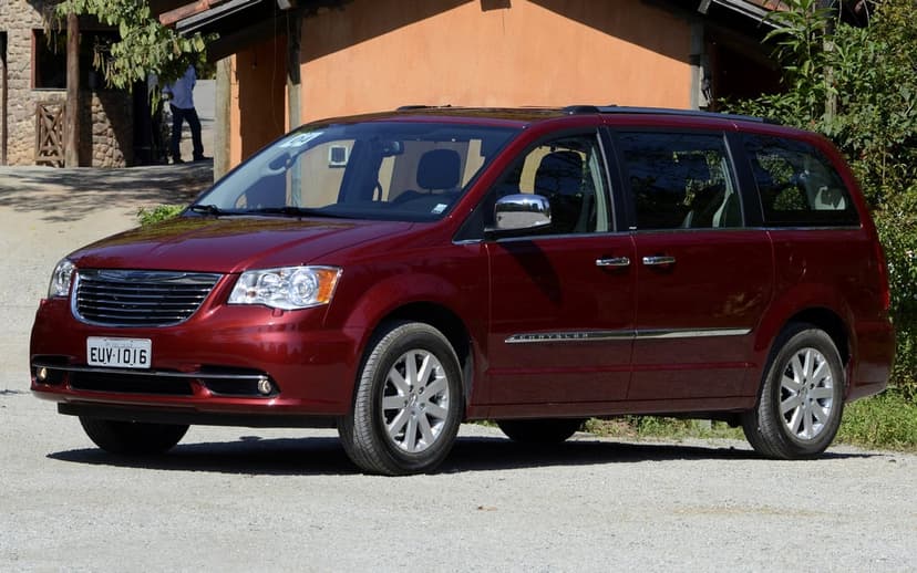 Red Chrysler minivan on a gravel driveway with a rustic orange building and green bushes in the background.